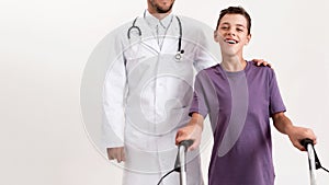 Cropped shot of male doctor helping teenaged disabled boy with cerebral palsy, taking steps using his walker 