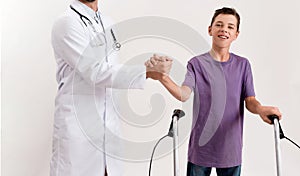 Cropped shot of male doctor shaking hands with teenaged disabled boy with cerebral palsy, taking steps using his walker