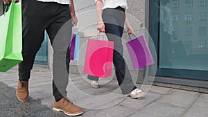 Cropped shot of male and female legs caucasian woman and african american man buyers walking in city street near store