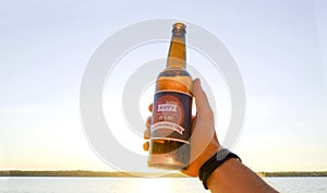 Cropped shot of male hand holding beer bottle against setting sun. Mississippi river background. Man celebrating independence day.