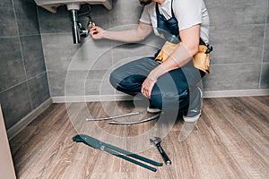 Cropped shot of male plumber with toolbelt repairing sink