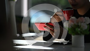 Cropped shot of man hand using smart phone and drinking hot coffee at office.