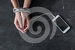 cropped shot of man with hands tied with smartphone wire, phone