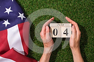 cropped shot of man holding calendar with 4th july date with american flag on green grass, americas independence