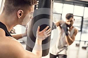 cropped shot of man holding punching bag while boxer hitting