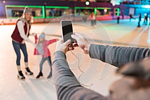 cropped shot of man holding smartphone with blank screen and photographing family skating