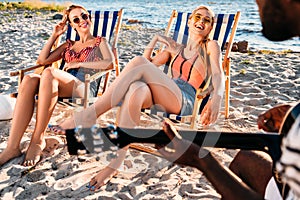 cropped shot of man playing guitar while girls resting in beach chairs