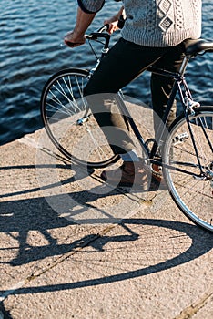 cropped shot of man standing on river shore with bicycle