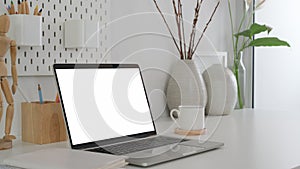 Cropped shot of modern designer workspace with mock up laptop, wooden figure and ceramic vase