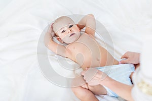 Cropped shot of mother changing diaper of adorable baby boy lying on bed