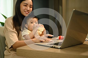 Cropped shot mother working with laptop at home with little baby son. Motherhood and child care concept