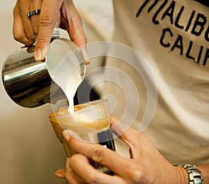 Cropped shot of movement hand barista making. Focus on hands holding cup of coffee and milk jar.