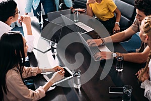 cropped shot of multicultural business partners having meeting at table with laptops in modern