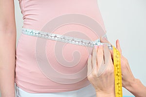 cropped shot of obstetrician gynecologist measuring belly size of pregnant woman with measuring tape