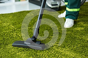 cropped shot of person cleaning green carpet with vacuum