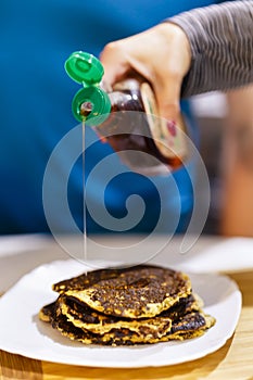 Cropped shot of person pouring maple syrup onto stack of pancake