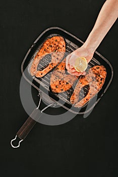 cropped shot of person squeezing lemon juice above salmon steaks on grill
