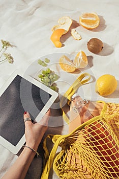 cropped shot of person using digital tablet and string bag with glass bottle