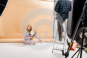 cropped shot of photographer standing on step ladder while beautiful girl posing with bouquet of flowers