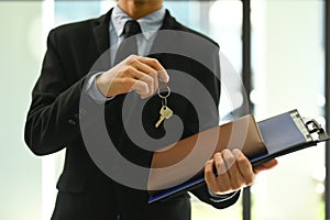 Cropped shot of professional male realtor or broker holding keys and contract document. Real estate service concept