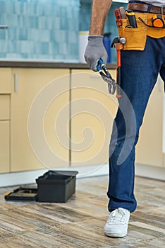 Cropped shot of repairman, plumber wearing a toolbelt holding a pipe wrench while getting ready for fixing a sink in the