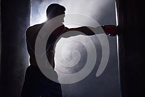 Working on his technique. Cropped shot of a silhouetted young male boxer working out on a punching bag in the gym.