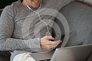 Smiling man using smart phone and laptop computer on sofa.