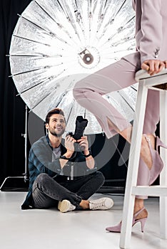 cropped shot of smiling photographer sitting and photographing stylish model
