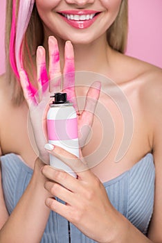 cropped shot of smiling young woman holding spray paint for hair in front of hand covered with pink paint