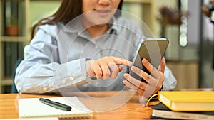 Cropped shot of smiling young woman typing typing text message on mobile phone while sitting at her office desk