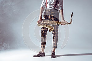 cropped shot of stylish young musician standing and holding saxophone in smoke