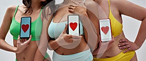 Cropped shot of three women wearing colorful underwear, holding smartphone with red heart shape on screen, posing