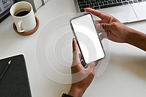 Cropped shot top view of businessman hands using smartphone mockup on office desk. Blank screen mobile phone for graphic display