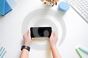 Cropped shot top view of women hands using smartphone mockup at the white desk. Blank screen mobile phone