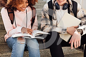 Cropped shot of two classmates sitting on stairs preparing assignments and smiling