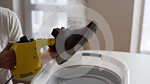 Cropped shot of unrecognizable young man disinfects inside of sneakers with hot steam using steam cleaner over basin at