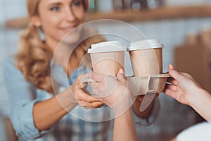 cropped shot of waitress and buyer holding coffee to go in paper