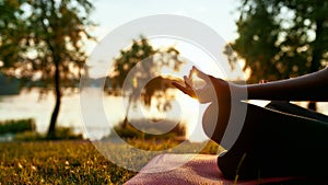 Cropped shot of a woman doing yoga outdoors near lake or river at sunrise in the morning, sitting in lotus pose on the