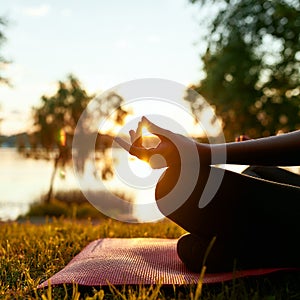 Cropped shot of a woman doing yoga outdoors near lake or river at sunrise in the morning, sitting in lotus pose on the