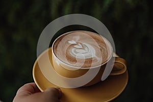 cropped shot of Woman holding cup of hot cappuccino on green background, top view.