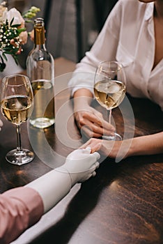 cropped shot of woman and mannequin holding hands at table with glasses of wine, unrequited