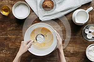 cropped shot of woman preparing ingredients for baking pancakes with sieve of flour