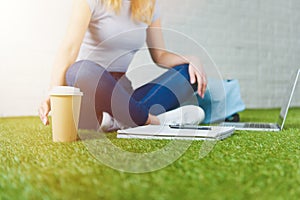 cropped shot of woman sitting on grass with cup of coffee to go and working