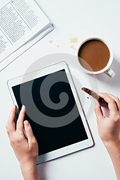 cropped shot of woman using tablet while eating chocolate chip cookie with coffee