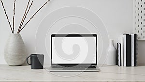 Cropped shot of workplace with blank screen laptop, decorations, books and coffee up on marble desk with white wall