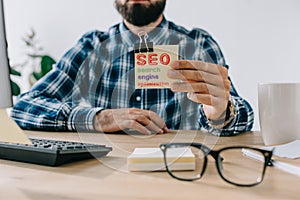 cropped shot of young bearded developer holding sticker with SEO - search