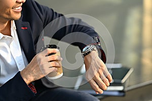 Cropped shot of young businessman sitting outdoors waiting for meeting and checking time looks at wristwatch