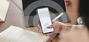 Cropped shot of young businesswoman using mock-up smartphone while working on her project in comfortable room