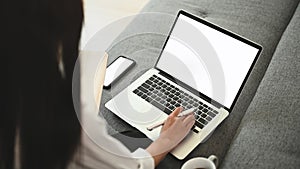 Cropped shot of young designer working with blank screen laptop computer on couch.