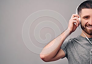 Cropped shot of a young handsome man who is holding white headphones, looking at the camera and smiling. Conceptual advertising.